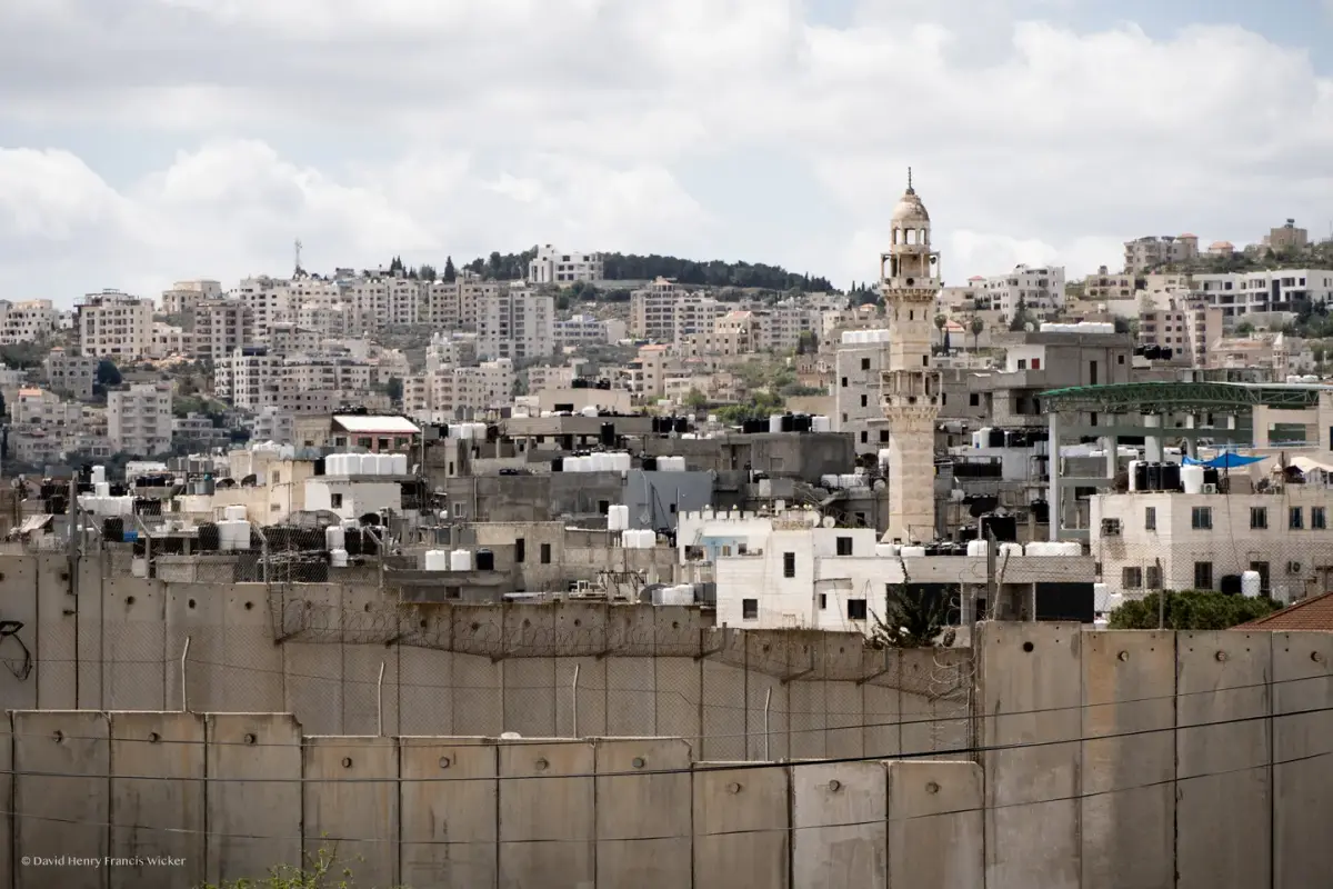 Bethlehem rises behind the concrete separation wall, with dense buildings extending across the hillside.